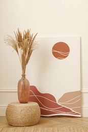Photo of Fluffy reed plumes and painting near white wall indoors. Interior elements