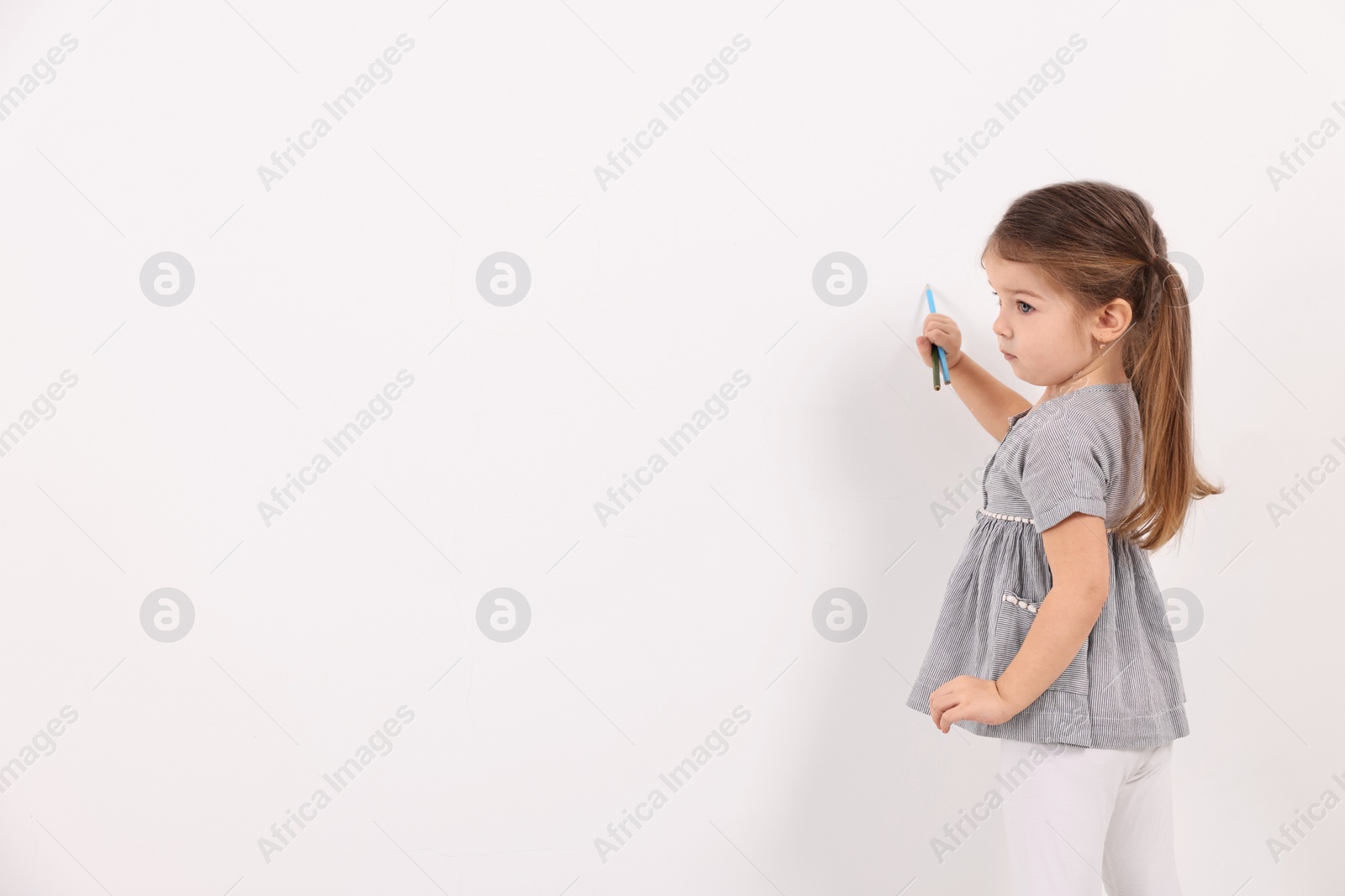 Photo of Little girl drawing with colorful pencils on white wall indoors. Space for text