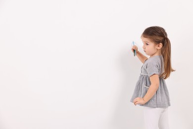 Little girl drawing with colorful pencils on white wall indoors. Space for text