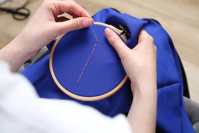 Photo of Woman with sewing needle and thread embroidering on cloth, closeup