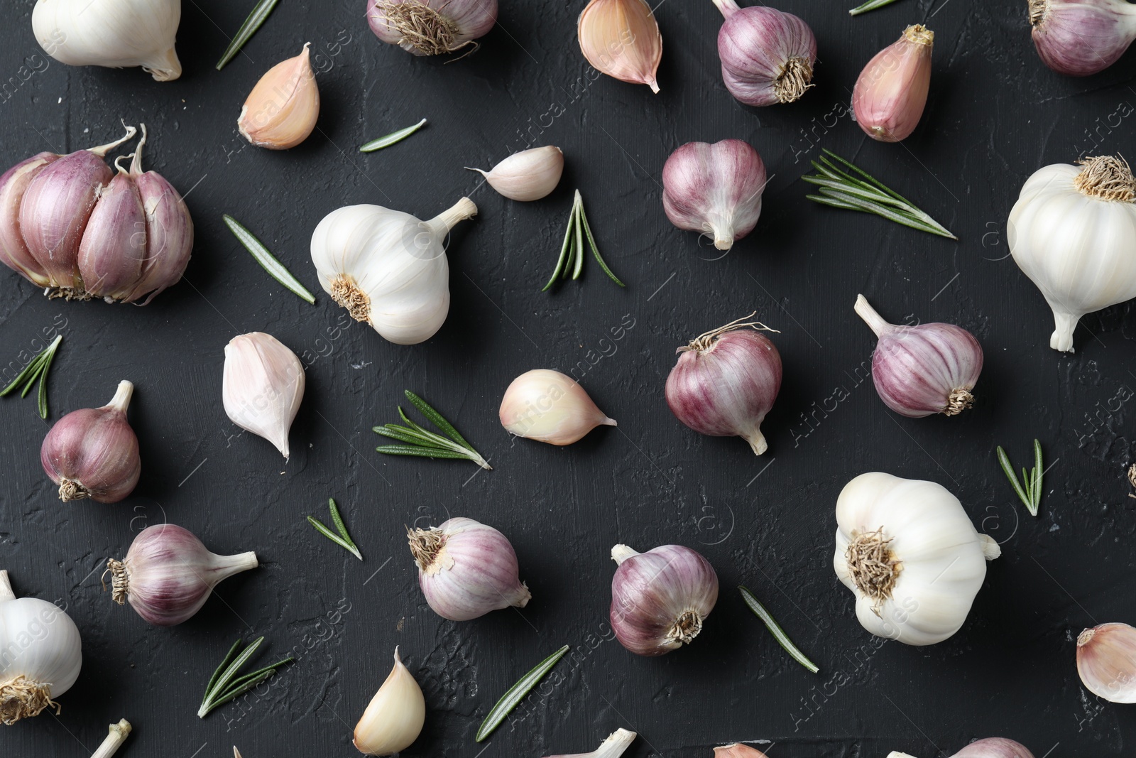 Photo of Fresh garlic and rosemary on dark textured table, flat lay