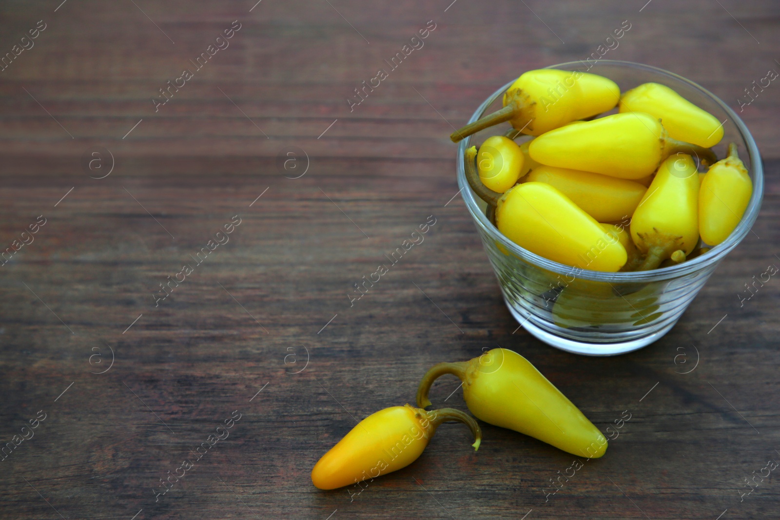 Photo of Glass bowl of pickled yellow jalapeno peppers on wooden table. Space for text