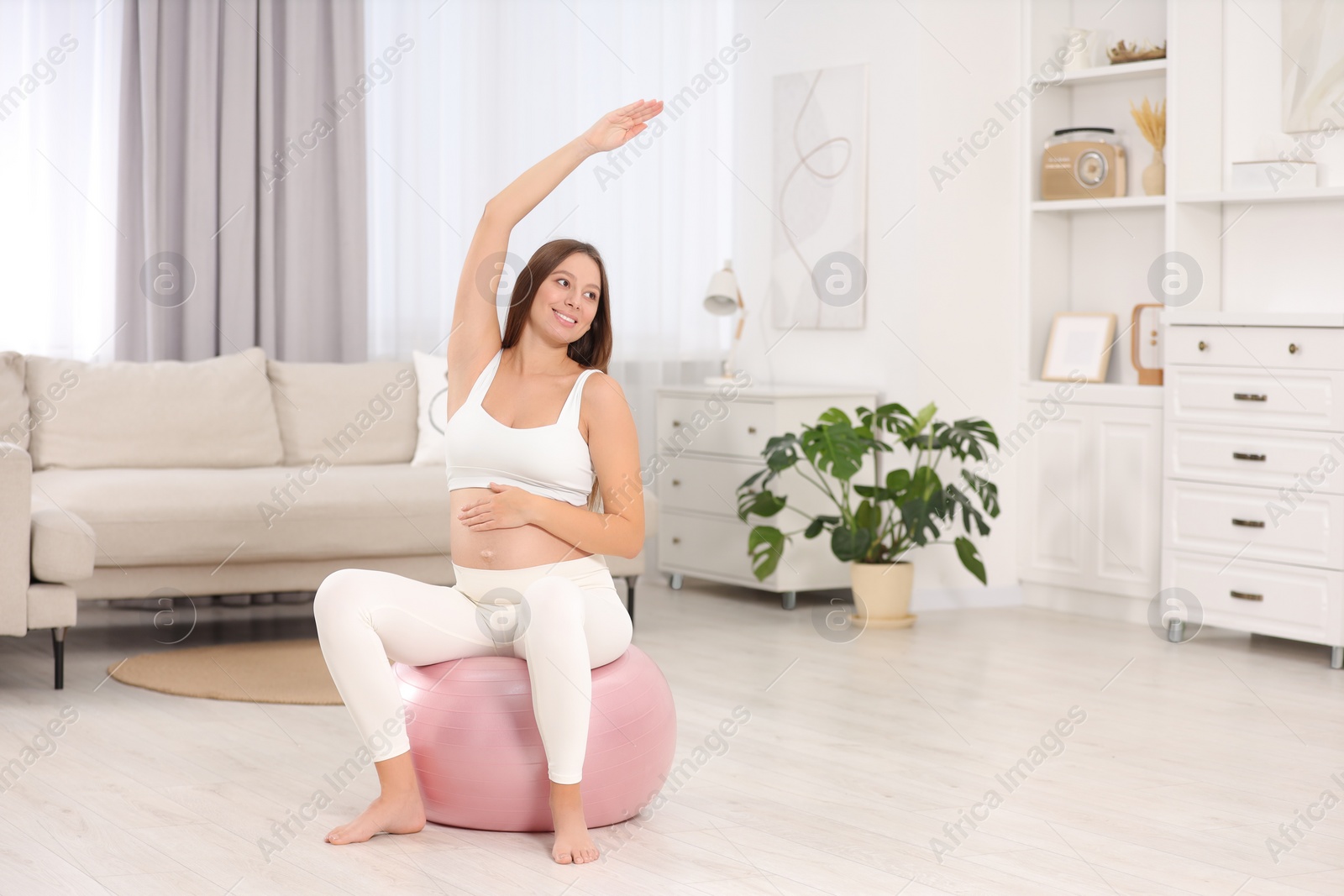 Photo of Pregnant woman doing exercises on fitness ball in room, space for text. Home yoga