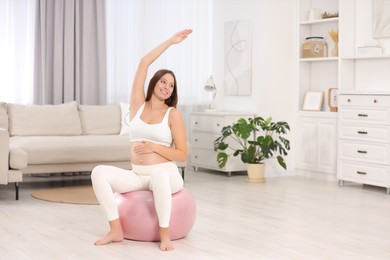 Pregnant woman doing exercises on fitness ball in room, space for text. Home yoga