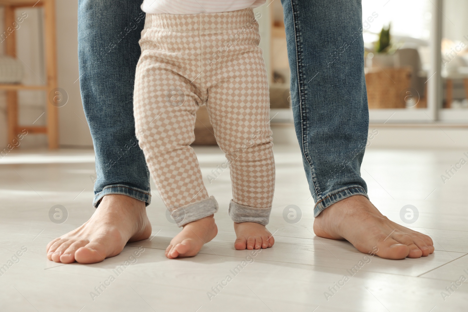 Photo of Father supporting his baby daughter while she learning to walk at home, closeup