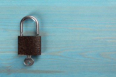 Modern padlock with key on light blue wooden table, top view. Space for text