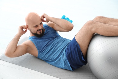 Photo of Overweight man doing exercise with fitness ball in gym
