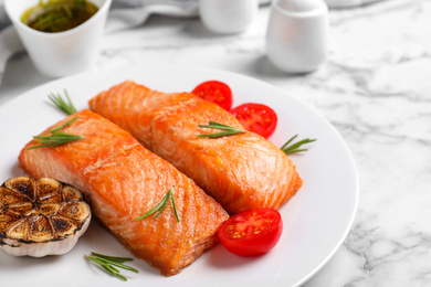 Photo of Delicious roasted fish served on white marble table, closeup