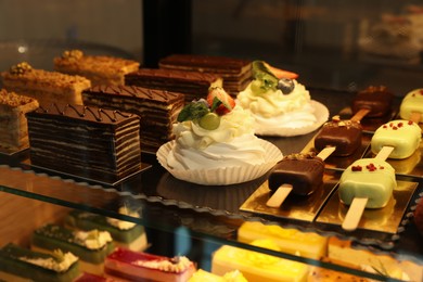 Photo of Showcase with different tasty desserts in bakery shop, closeup