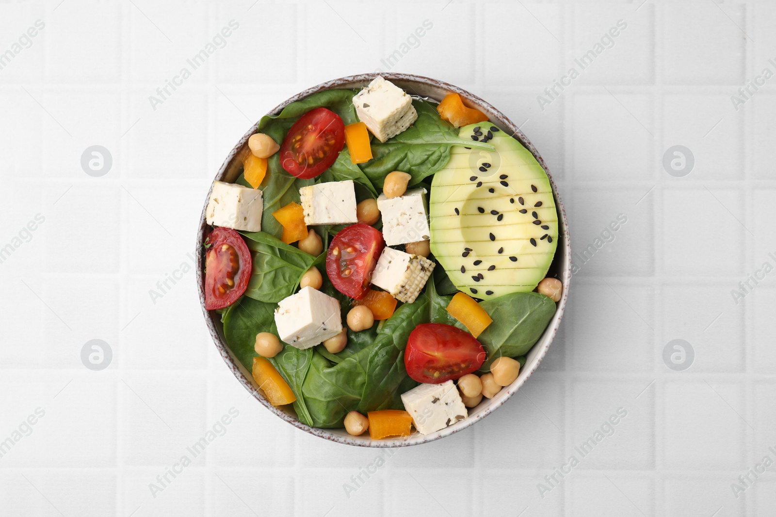 Photo of Bowl of tasty salad with tofu and vegetables on white tiled table, top view