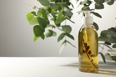 Photo of Bottle of liquid soap on white table near eucalyptus branches, space for text