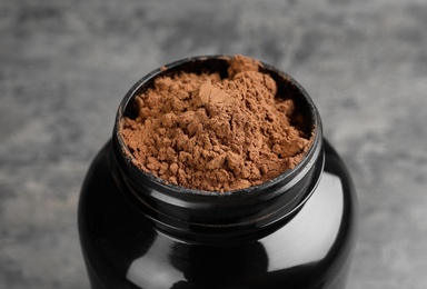 Photo of Black jar with chocolate protein powder on grey table, closeup