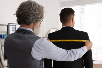 Professional tailor working with client in atelier, back view