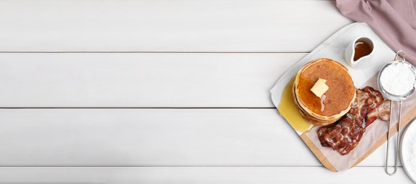 Delicious pancakes with maple syrup, butter and fried bacon on white wooden table, flat lay with space for text. Banner design