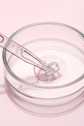 Glass pipette and petri dish with liquid on pink background