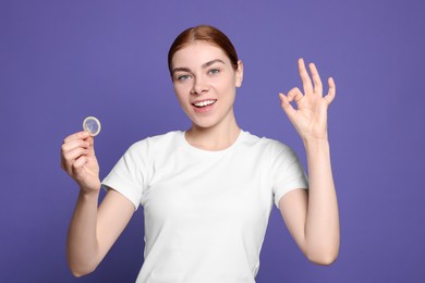 Photo of Woman with condom showing ok gesture on purple background. Safe sex