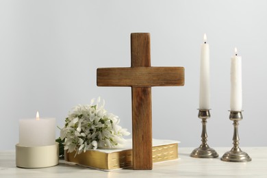 Burning church candles, wooden cross, Bible and flowers on white table