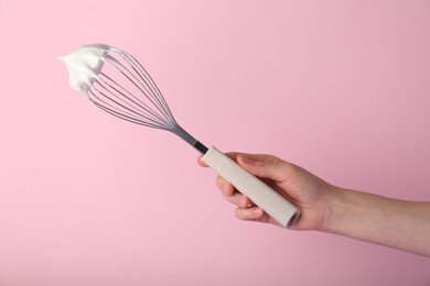 Photo of Woman holding whisk with whipped cream on pink background, closeup