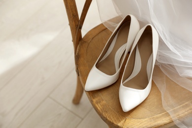 Photo of Pair of white wedding high heel shoes and veil on wooden chair indoors