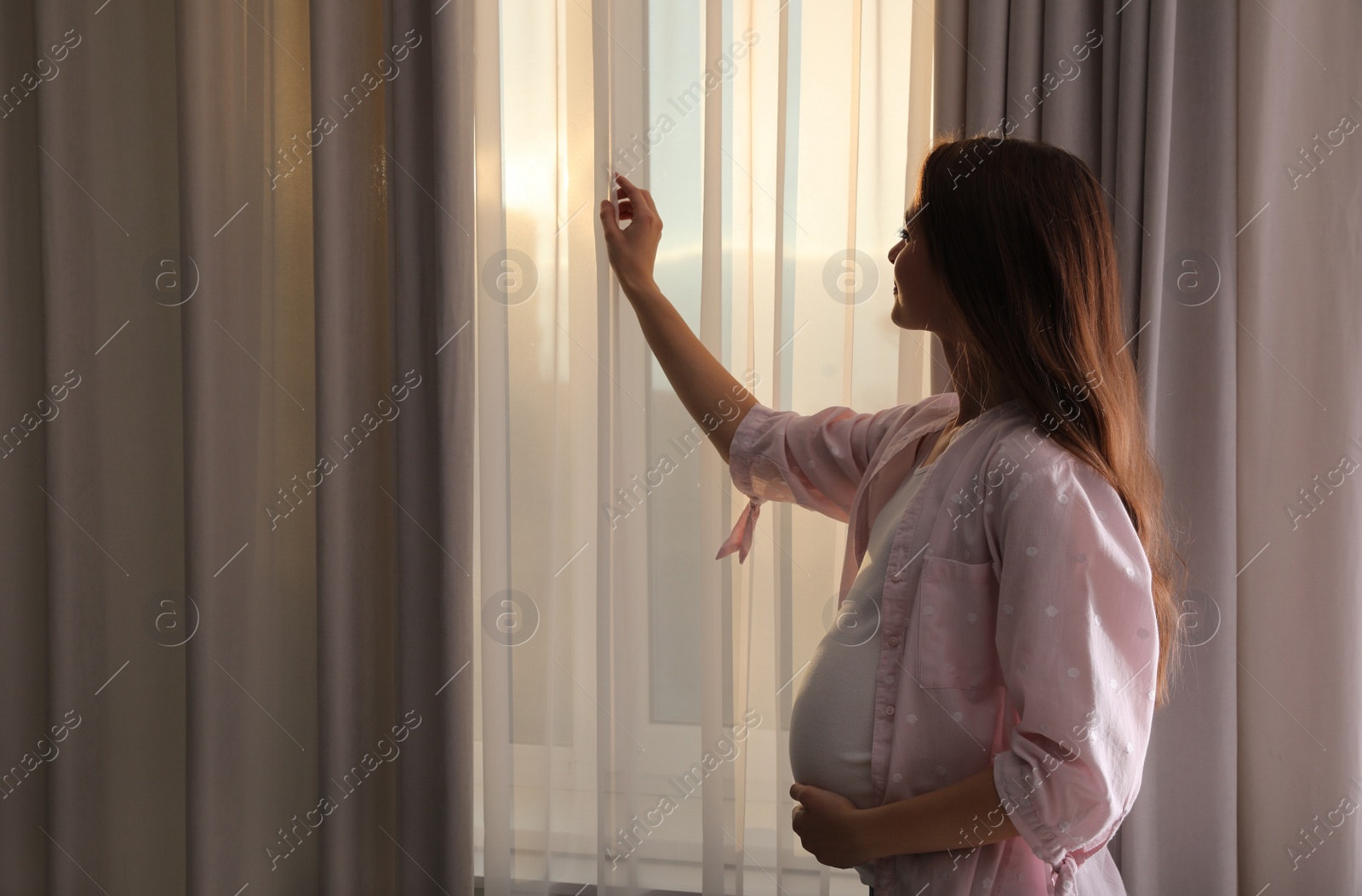 Photo of Young pregnant woman near window at home
