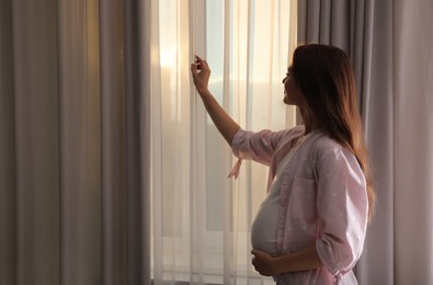 Photo of Young pregnant woman near window at home