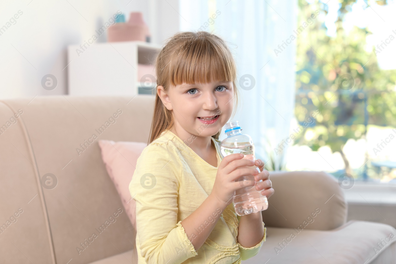 Photo of Cute little girl holding bottle with water indoors