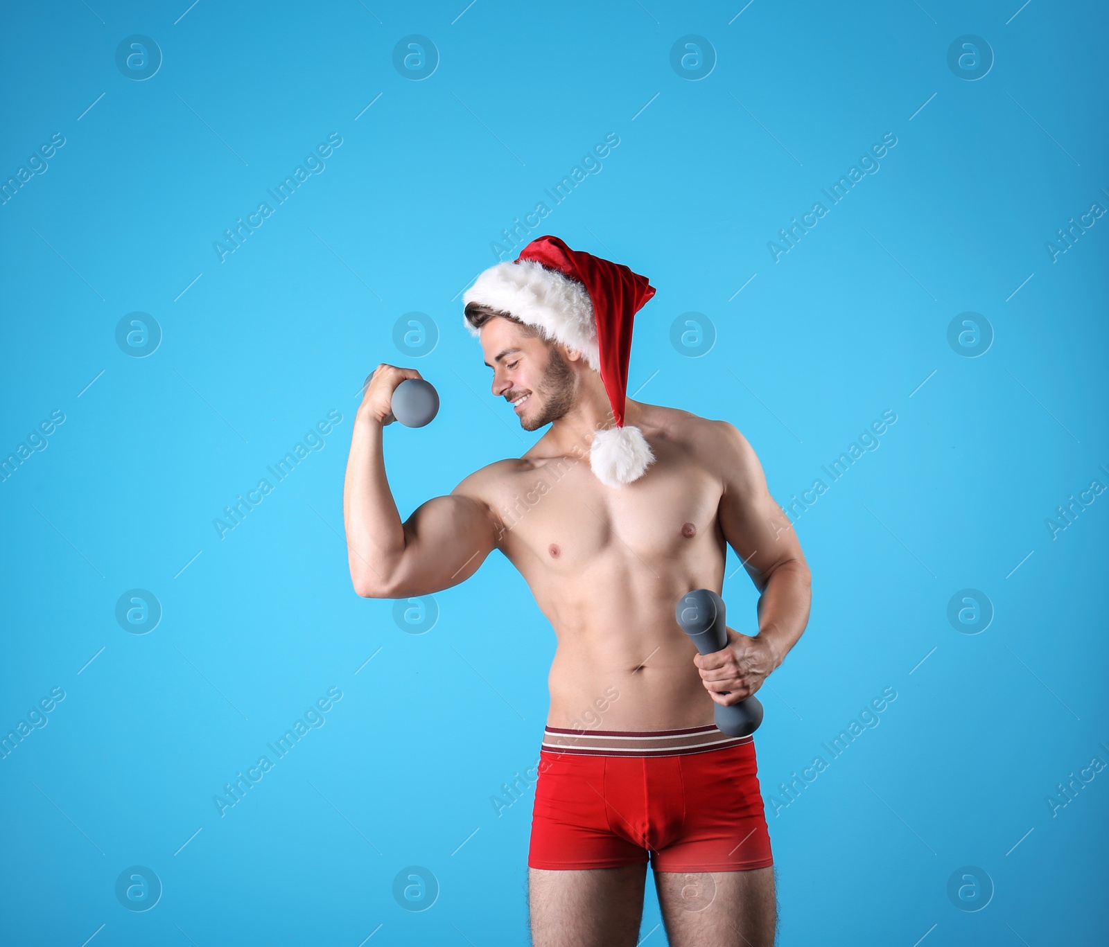 Photo of Shirtless sexy young Santa Claus with dumbbells on color background