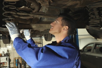 Photo of Professional mechanic fixing lifted car at automobile repair shop