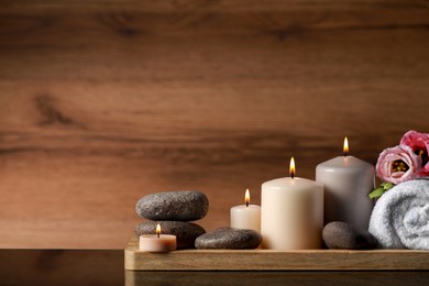Photo of Beautiful composition with spa stones, flowers and burning candles on mirror table against wooden background. Space for text