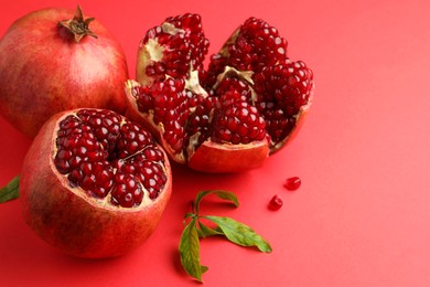 Photo of Fresh pomegranates and green leaves on red background, space for text