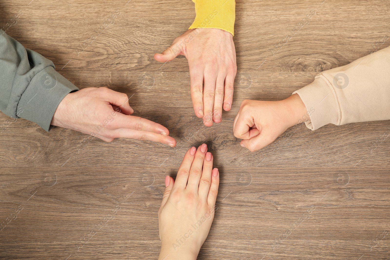 Photo of Closeup of people playing rock, paper and scissors on wooden background, top view