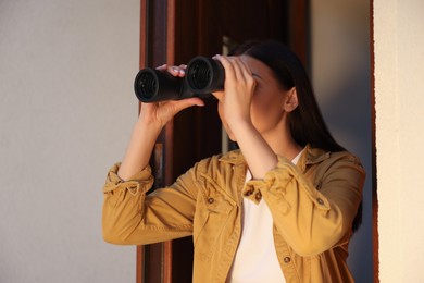 Photo of Concept of private life. Curious young woman with binoculars spying on neighbours outdoors