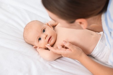 Photo of Woman applying cream onto baby`s face on bed, closeup