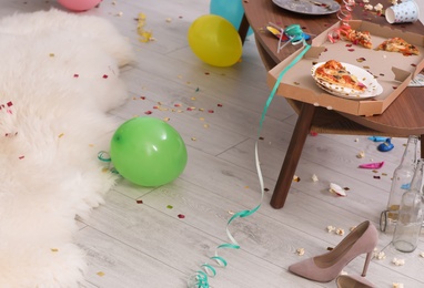 Photo of Table with pizza leftovers in messy room. After party chaos