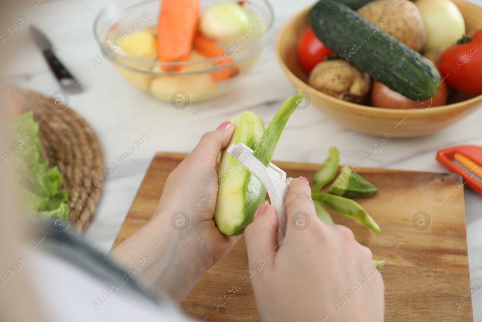 Photo of Woman peeling fresh zucchini at white marble table, closeup