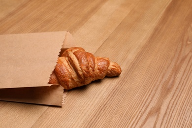 Paper bag with delicious croissant on wooden background. Space for text