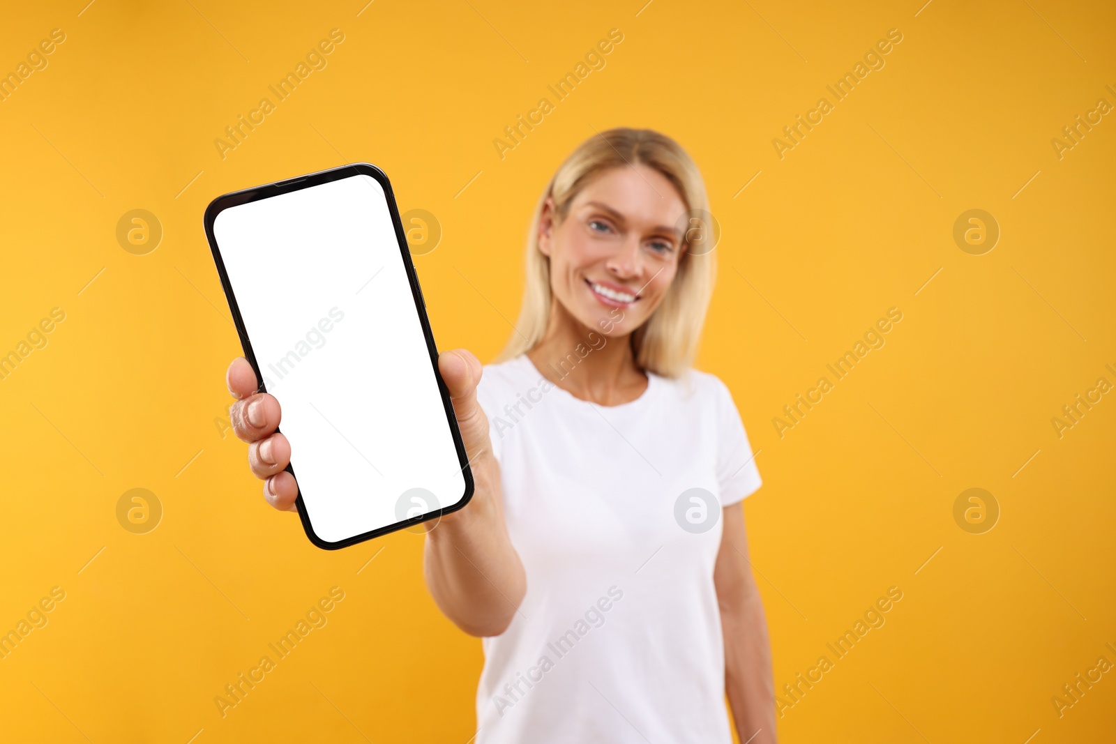 Photo of Happy woman holding smartphone with blank screen on orange background, selective focus