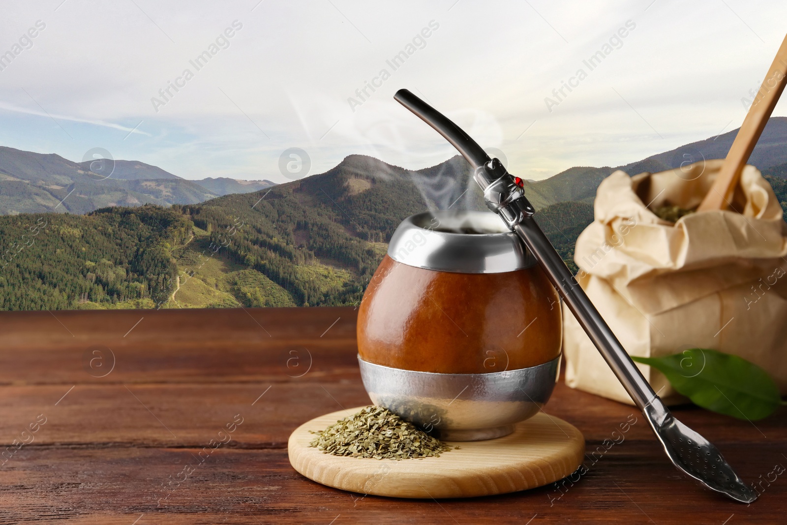 Image of Calabash with mate tea and bombilla on wooden table and beautiful view of mountain landscape, space for text