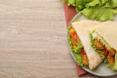 Photo of Delicious pita sandwiches with fried fish, pepper, tomatoes and lettuce on wooden table, flat lay. Space for text