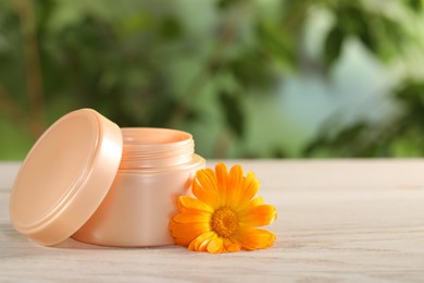 Jar of cream and beautiful calendula flower on white wooden table outdoors, closeup. Space for text
