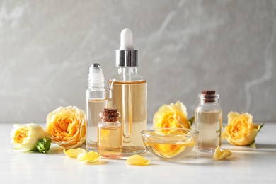 Bottles of rose essential oil and fresh flowers on white table