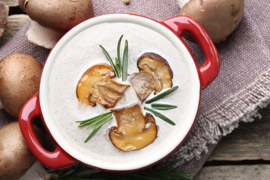 Delicious homemade mushroom soup in ceramic pot and fresh ingredients on wooden table, flat lay