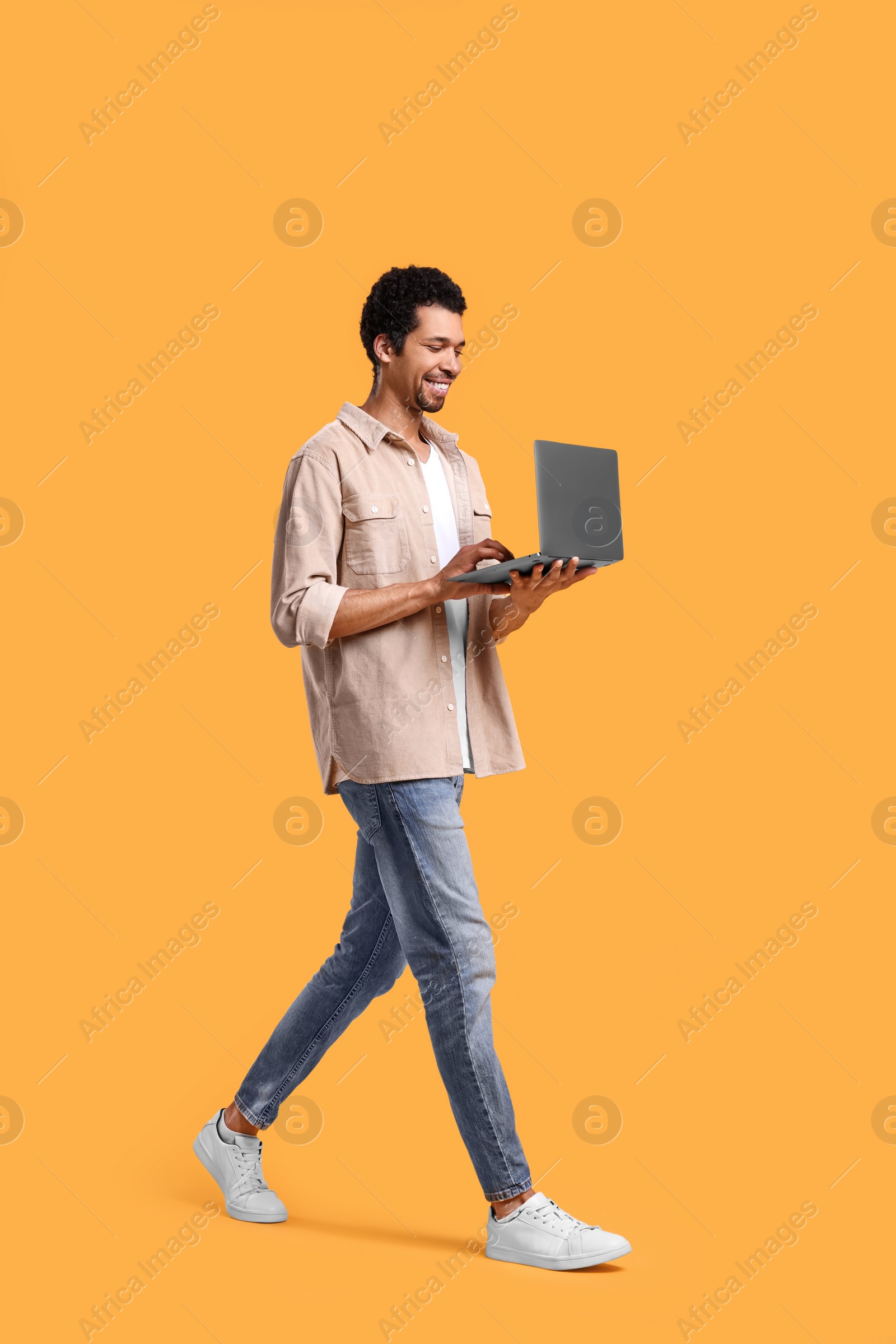 Photo of Happy man with laptop walking on orange background