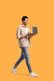 Happy man with laptop walking on orange background