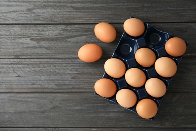 Raw chicken eggs in ceramic holder on wooden background, top view. Space for text