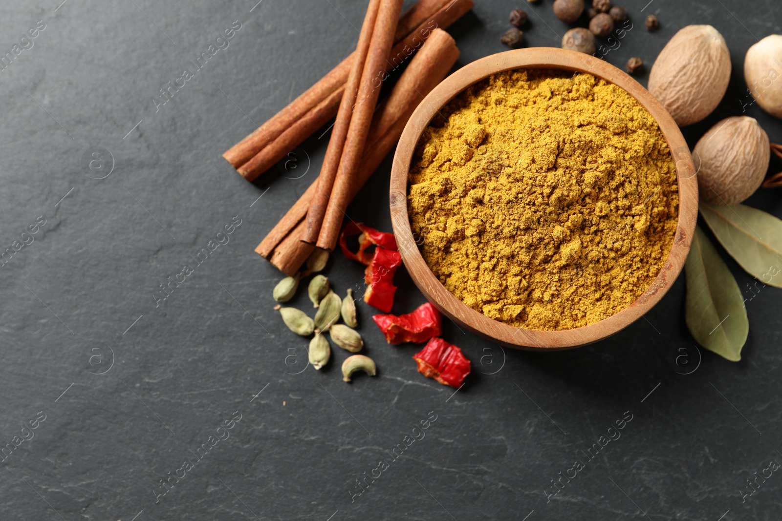 Photo of Dry curry powder in bowl and other spices on dark textured table, flat lay. Space for text