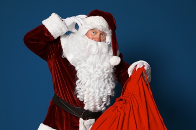 Photo of Authentic Santa Claus with bag full of gifts on blue background