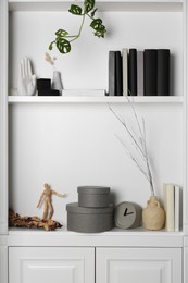 White shelves with books, clock and different decor indoors. Interior design