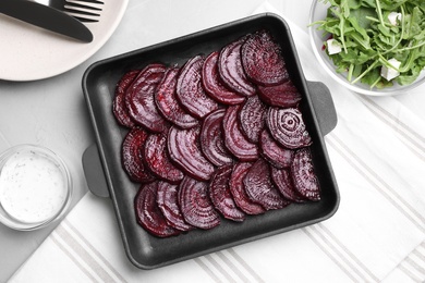 Baking dish with roasted beetroot slices on light grey table, flat lay