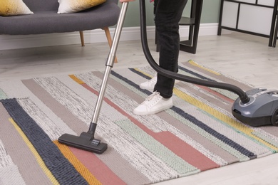 Young man removing dirt from carpet with vacuum cleaner at home